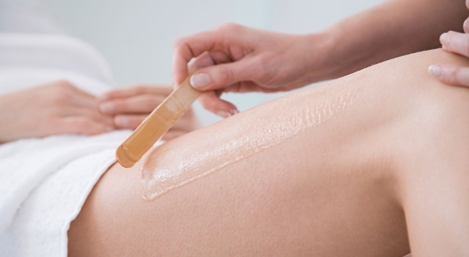 Student spa waxing service — warm wax applied to a client's leg with a wooden spatula